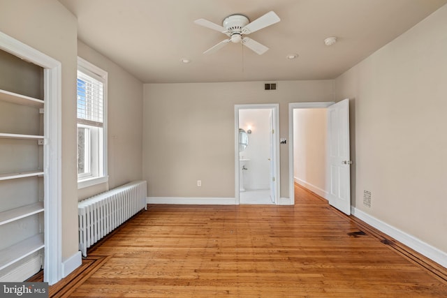 unfurnished bedroom featuring multiple windows, ensuite bath, light hardwood / wood-style flooring, and radiator heating unit