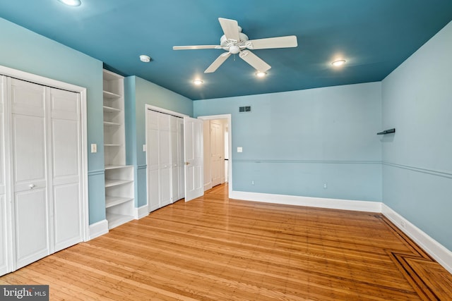 unfurnished bedroom featuring light hardwood / wood-style floors, multiple closets, and ceiling fan