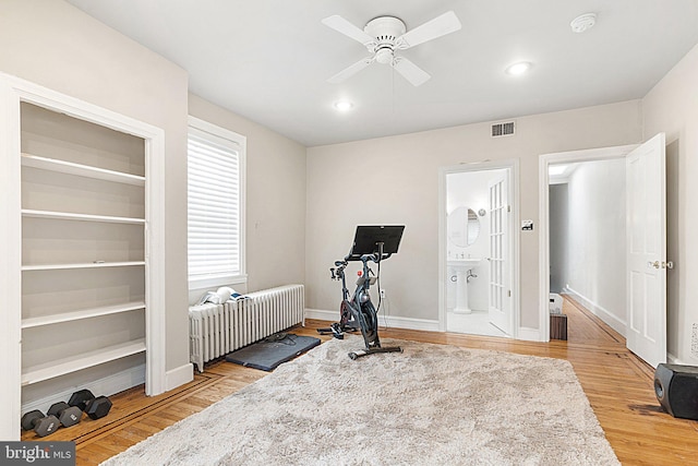 exercise room with ceiling fan, light hardwood / wood-style flooring, and radiator heating unit