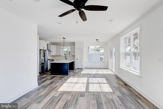 unfurnished living room featuring crown molding, ceiling fan, sink, and light wood-type flooring