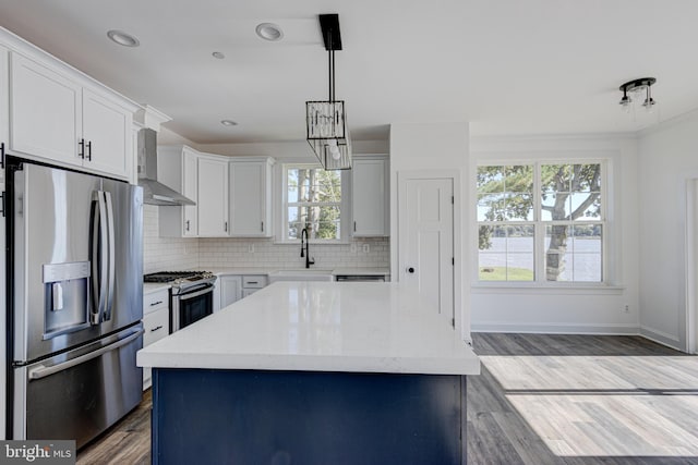 kitchen featuring wall chimney range hood, sink, appliances with stainless steel finishes, white cabinetry, and a center island