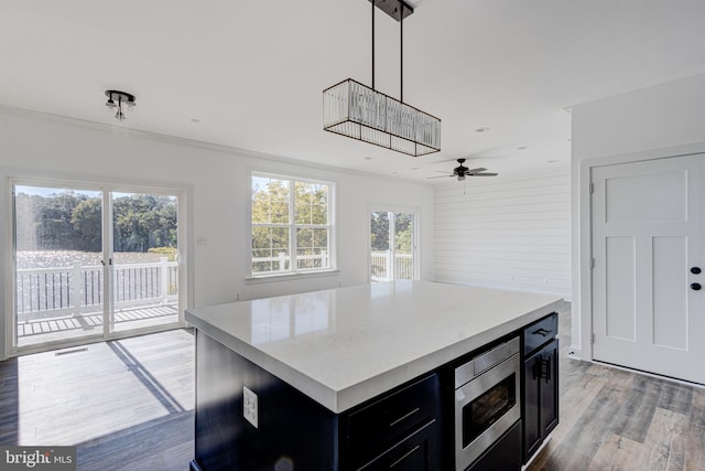 kitchen with crown molding, wood-type flooring, a center island, hanging light fixtures, and stainless steel microwave