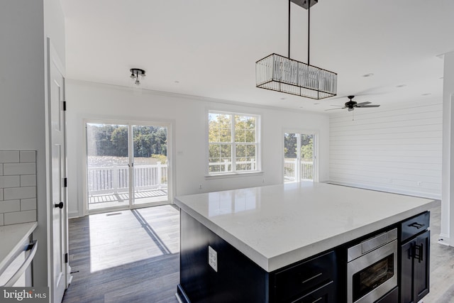 kitchen with hardwood / wood-style floors, a center island, stainless steel microwave, ornamental molding, and decorative light fixtures