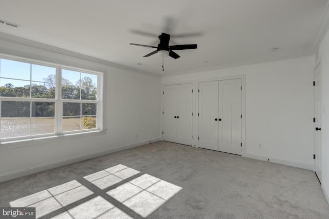 unfurnished bedroom with light colored carpet, ornamental molding, and multiple closets