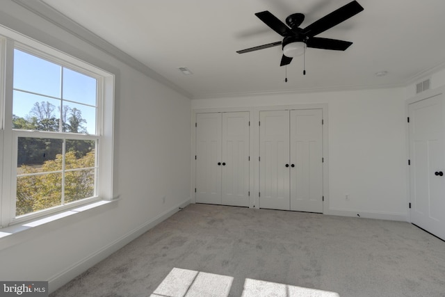 unfurnished bedroom with multiple closets, crown molding, light colored carpet, and ceiling fan