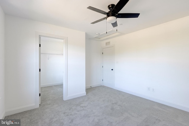 unfurnished bedroom with a walk in closet, light colored carpet, a closet, and ceiling fan