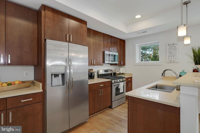 kitchen featuring sink, light wood-type flooring, hanging light fixtures, and appliances with stainless steel finishes