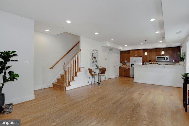 kitchen with appliances with stainless steel finishes, kitchen peninsula, light wood-type flooring, and decorative light fixtures