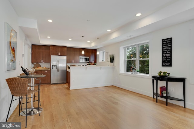 kitchen with pendant lighting, appliances with stainless steel finishes, a tray ceiling, kitchen peninsula, and light wood-type flooring