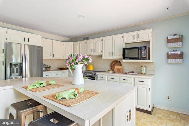 kitchen featuring a breakfast bar area, appliances with stainless steel finishes, ornamental molding, white cabinets, and decorative backsplash