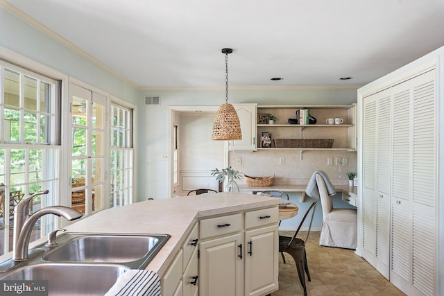 kitchen with white cabinetry, hanging light fixtures, crown molding, and sink