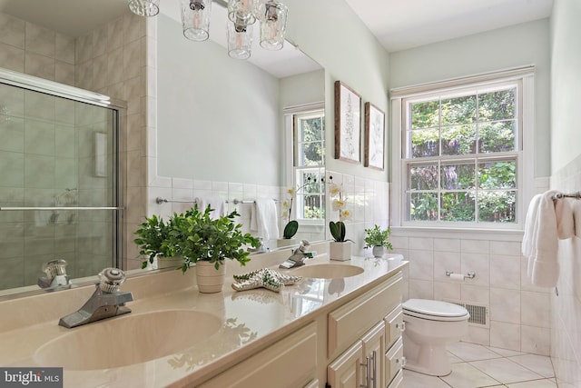 bathroom with tile walls, vanity, toilet, a shower with door, and tile patterned floors