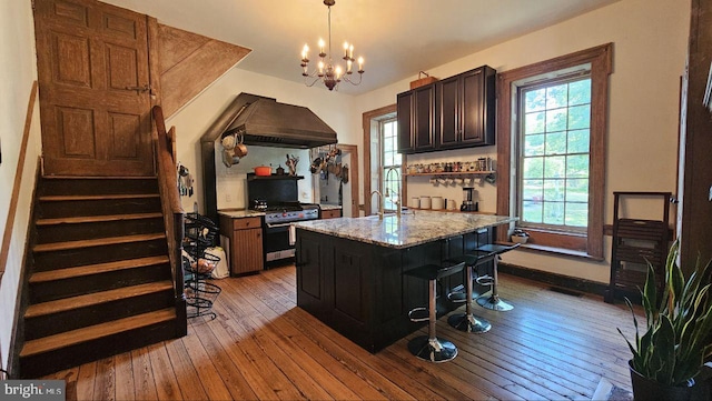 kitchen with custom range hood, light hardwood / wood-style floors, a breakfast bar, stainless steel range with gas cooktop, and a kitchen island with sink