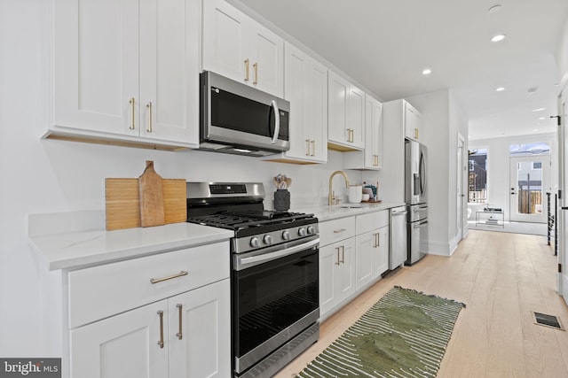 kitchen featuring light stone counters, appliances with stainless steel finishes, white cabinetry, light wood-type flooring, and sink