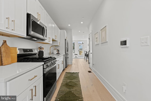 kitchen with appliances with stainless steel finishes, sink, light wood-type flooring, and white cabinets