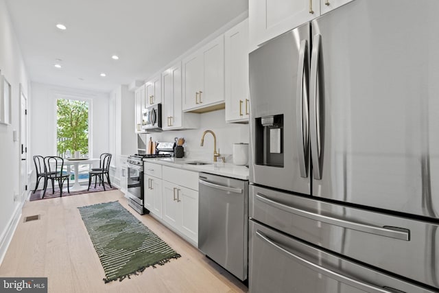 kitchen featuring appliances with stainless steel finishes, sink, light stone countertops, white cabinetry, and light hardwood / wood-style flooring