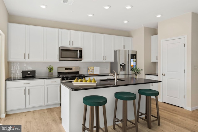 kitchen featuring a kitchen island with sink, light wood-type flooring, white cabinets, and appliances with stainless steel finishes