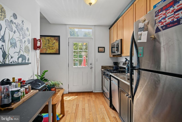 kitchen with appliances with stainless steel finishes, light hardwood / wood-style floors, and dark stone counters