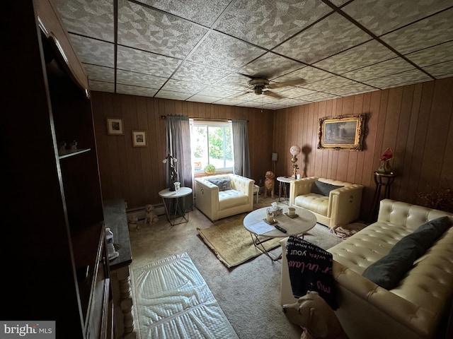 carpeted living room with wood walls, baseboard heating, and ceiling fan