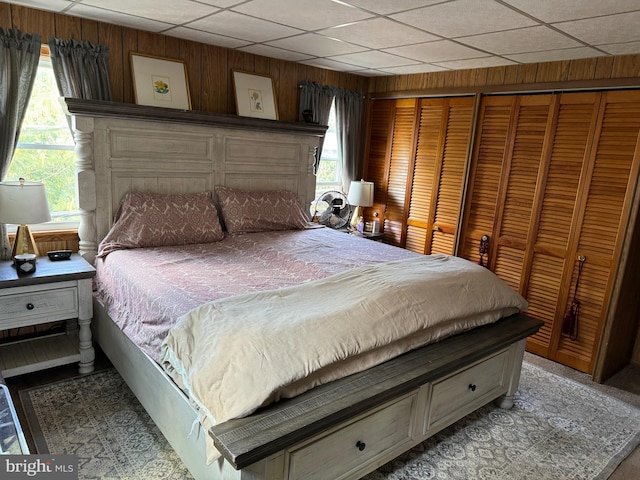 bedroom featuring a drop ceiling, wooden walls, and multiple closets