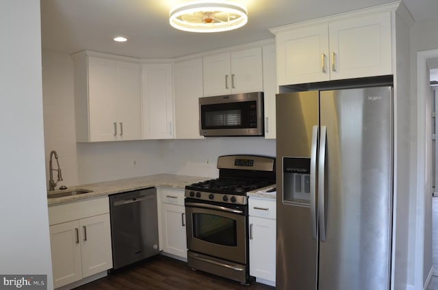 kitchen featuring stainless steel appliances, sink, light stone countertops, white cabinetry, and dark hardwood / wood-style flooring