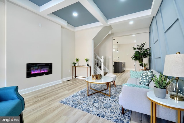 living area featuring stairway, baseboards, light wood-style floors, and coffered ceiling