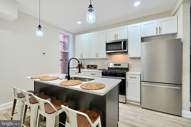 kitchen with light countertops, light wood-style flooring, appliances with stainless steel finishes, hanging light fixtures, and a sink