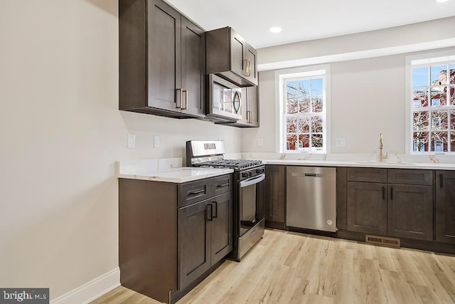 kitchen with light countertops, light wood-style flooring, appliances with stainless steel finishes, a sink, and dark brown cabinets