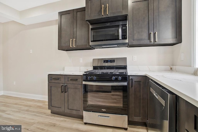 kitchen with light stone counters, stainless steel appliances, light wood-style flooring, dark brown cabinetry, and baseboards