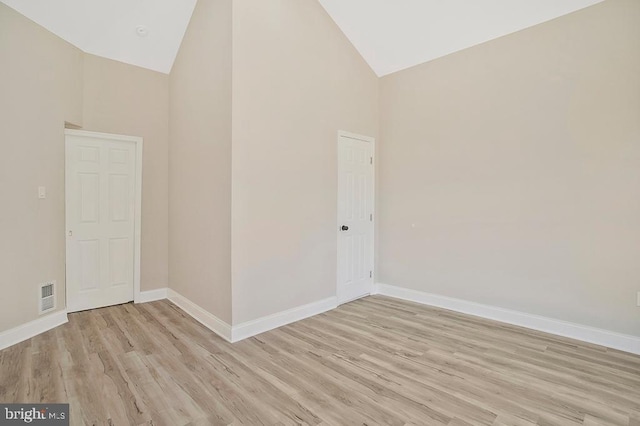 empty room with high vaulted ceiling, light wood-style flooring, visible vents, and baseboards