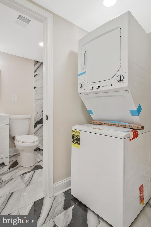 clothes washing area featuring laundry area, baseboards, visible vents, stacked washer / drying machine, and marble finish floor