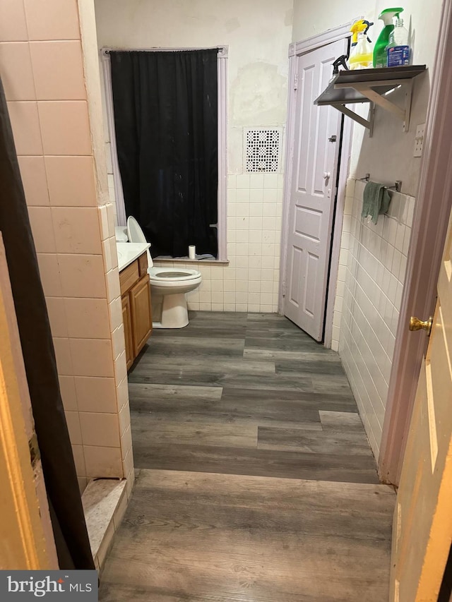 bathroom featuring walk in shower, toilet, vanity, tile walls, and hardwood / wood-style floors