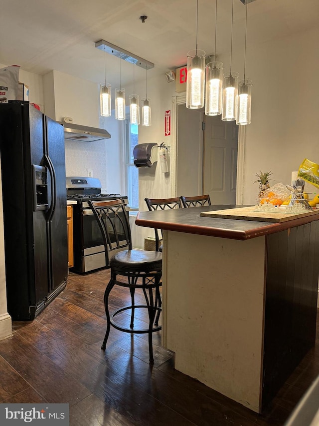 kitchen featuring stainless steel gas stove, dark hardwood / wood-style flooring, black fridge, and wall chimney exhaust hood