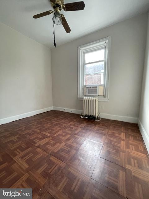 unfurnished room with cooling unit, ceiling fan, radiator, and dark parquet floors