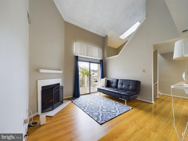 living room with a skylight, a textured ceiling, light hardwood / wood-style flooring, and high vaulted ceiling