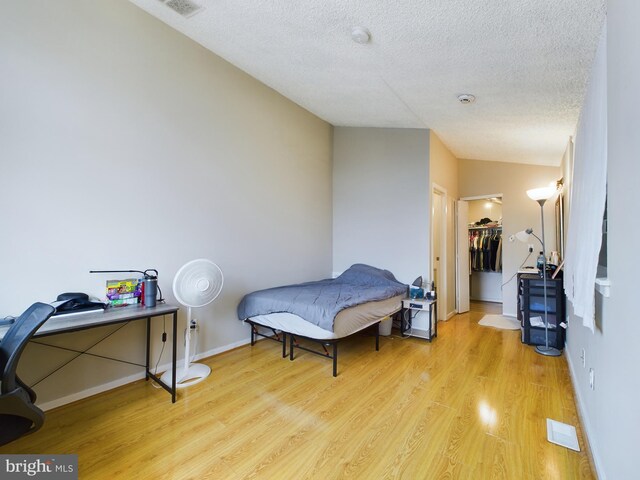 bedroom with a textured ceiling, a walk in closet, light hardwood / wood-style flooring, and a closet