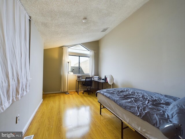 bedroom with lofted ceiling, light hardwood / wood-style floors, and a textured ceiling