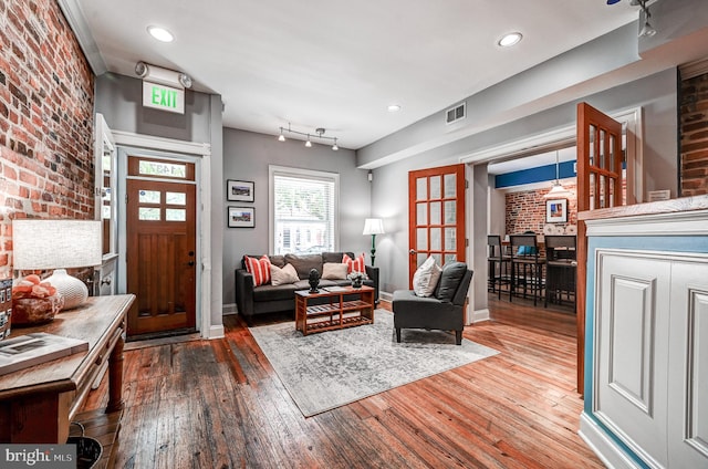 living room with hardwood / wood-style flooring, track lighting, and brick wall