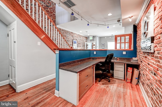 office space with built in desk, light wood-type flooring, and brick wall