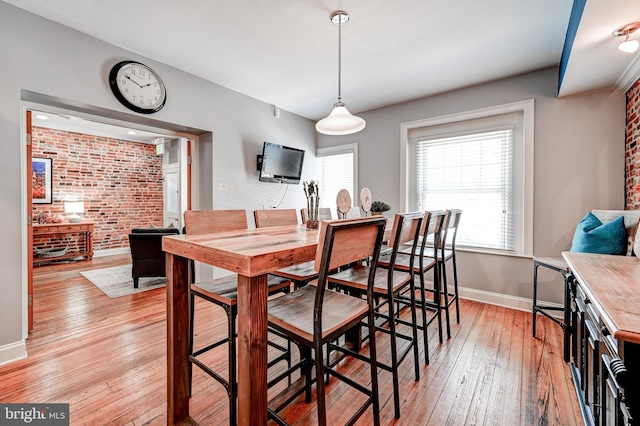 dining space with brick wall and light wood-type flooring