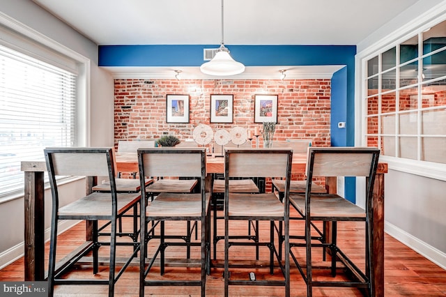 dining area with wood-type flooring and brick wall