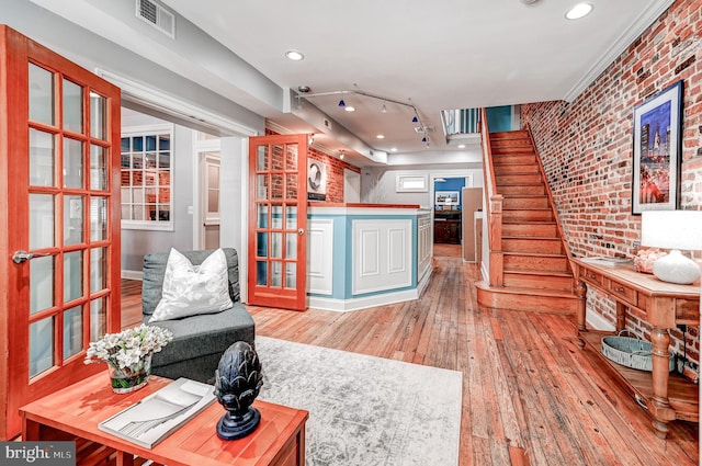 living room with brick wall, rail lighting, and light hardwood / wood-style flooring