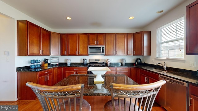 kitchen with sink, dark stone countertops, stainless steel appliances, a kitchen breakfast bar, and light wood-type flooring