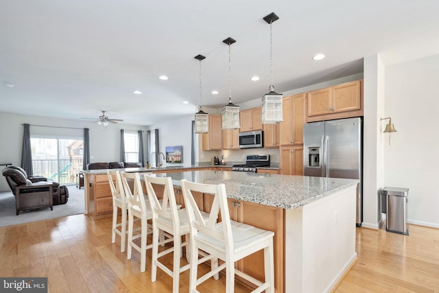 kitchen with a breakfast bar area, light wood-style flooring, appliances with stainless steel finishes, open floor plan, and a peninsula