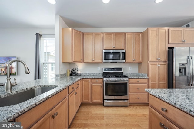 kitchen featuring light wood-type flooring, light stone countertops, stainless steel appliances, and a sink