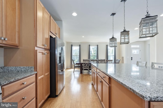 kitchen with pendant lighting, stainless steel refrigerator with ice dispenser, light wood finished floors, a kitchen island, and a kitchen bar