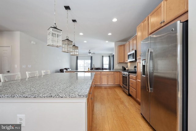 kitchen with a center island, decorative light fixtures, light wood finished floors, stainless steel appliances, and a kitchen breakfast bar