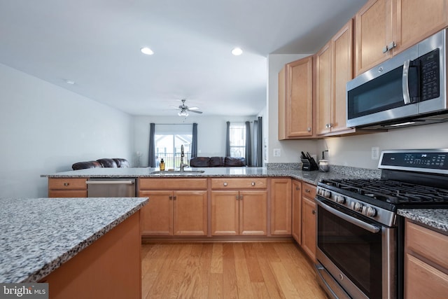 kitchen featuring a sink, open floor plan, appliances with stainless steel finishes, light wood-type flooring, and light stone countertops