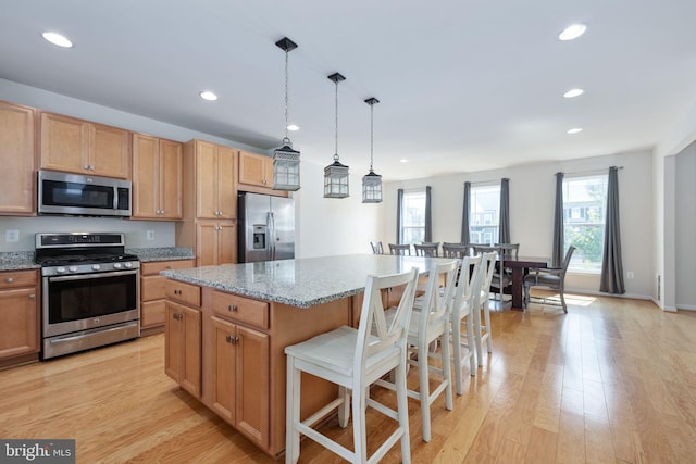 kitchen with light wood-type flooring, a kitchen island, stainless steel appliances, and decorative light fixtures