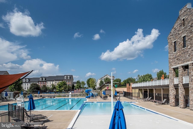 community pool featuring a patio, a water slide, and fence